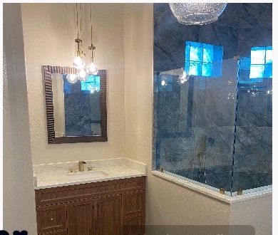 Custom master vanity with brushed-brass chandelier and frameless glass shower