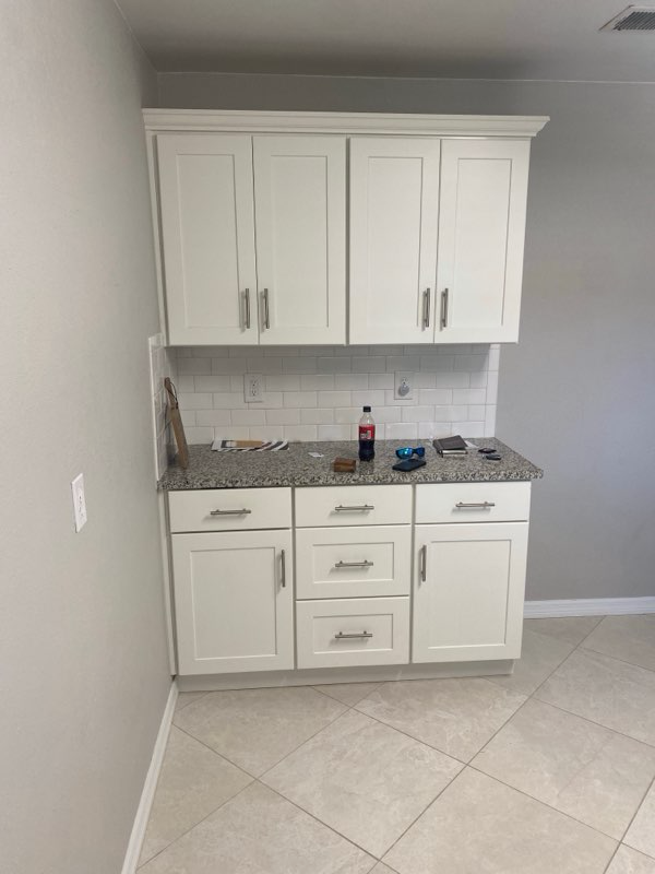 Custom wet bar with white shaker cabinets, stone counter, and subway tile